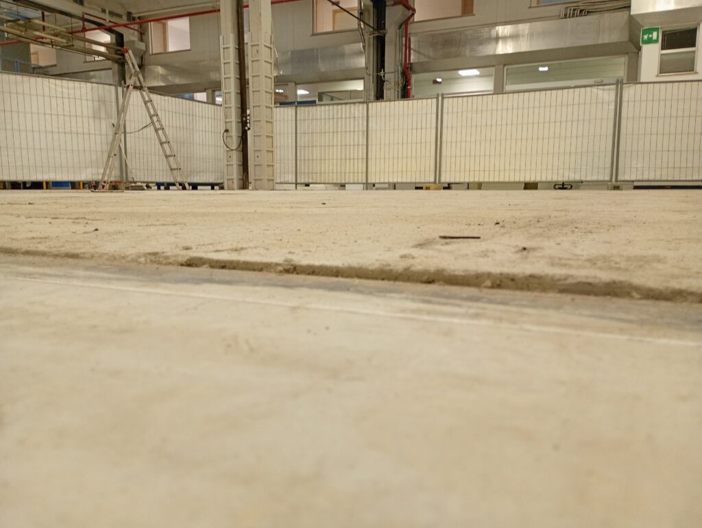 Pavimento industriale in calcestruzzo grezzo e disconnesso prima dell'intervento